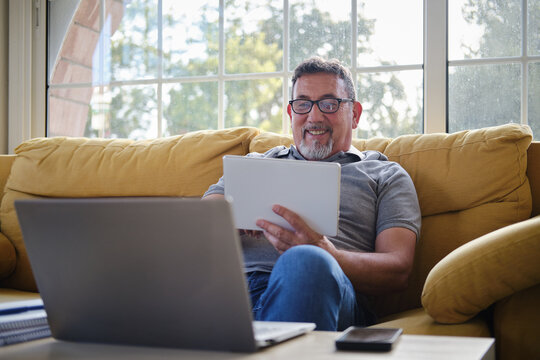 Mature man relaxing on sofa using digital tablet