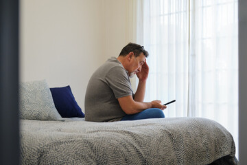 Mature man feeling stressed checking phone in bed