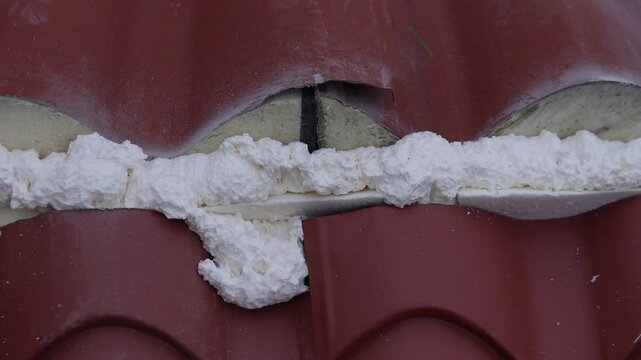 Thermal insulation material. Sealing or filling roof cracks with foam. Corrugated roofing panels of a dark red color, similar to metal tiles, ondulin, and corrugated sheets.
