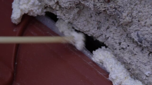 Thermal insulation material. Sealing or filling roof cracks with foam. Corrugated roofing panels of a dark red color, similar to metal tiles, ondulin, and corrugated sheets.