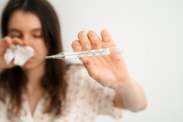 Woman showing thermometer while wiping nose