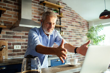 Senior man happily greeting on video call in home kitchen