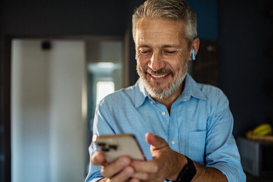 Mature man smiling at smartphone with earbuds at home