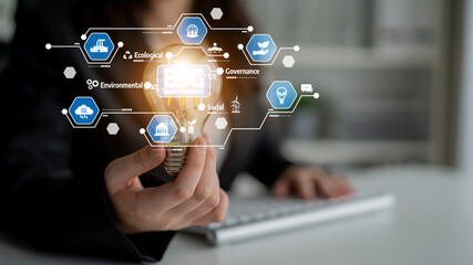 A business professional holds a glowing light bulb symbolizing innovative ideas while digital icons illustrate environmental, social, and governance concepts in an office setting. Tessel