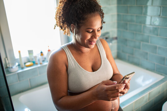 Happy adult pregnant woman using smartphone in home bathroom - Powered by Adobe