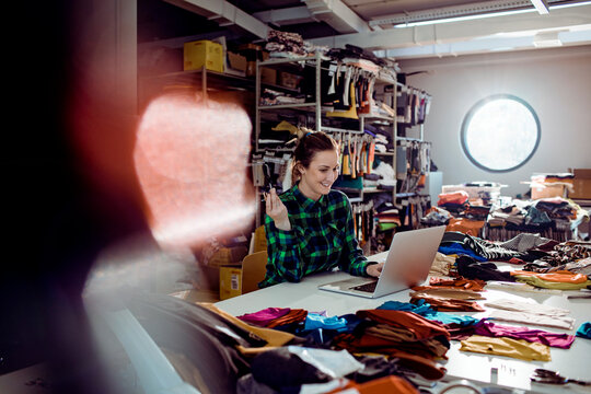 Young adult woman smiling while working on laptop in fabric workshop