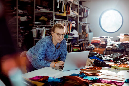 Young adult woman focused on laptop in textile studio