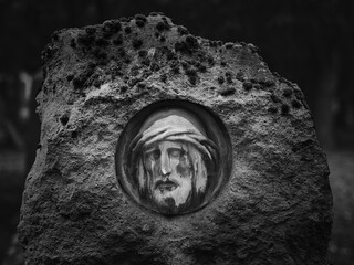 Stone relief of Christ&rsquo;s face embedded in a weathered rock, photographed in black and white