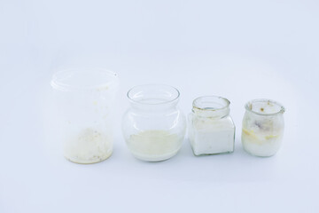 A row of four transparent containers filled with spoiled dairy products is displayed on a clean white background. Each jar shows different stages of decay, including separation, discoloration