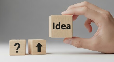Hand holding wooden block with idea text next to arrow and question mark blocks symbolizing growth solution and creativity