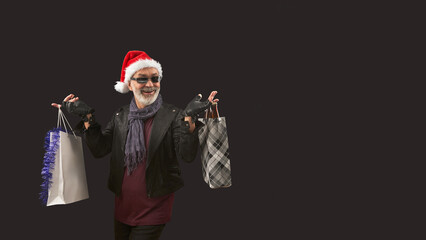 Portrait of happy Santa in black jacket and leather gloves with shopping bags and bottles of beer in his hands on dark burgundy background.