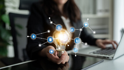 A businesswoman is holding a light bulb that symbolizes innovation, surrounded by digital icons....