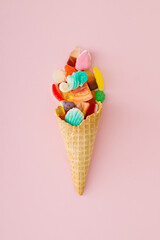 Gummy candies in waffle ice cream cone on pastel pink background. Creative candy dessert concept. Minimal trendy gummies layout. Ice cream and jelly sweets aesthetic. Colorful flat lay. Top view.