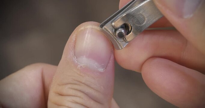 A man cuts his fingernails using a metal nail clipper