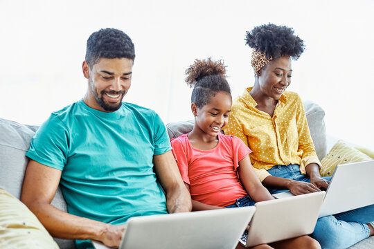 Mother, father and daughter doing homework with laptop at home. Mom, dad and teenage black girl happy using laptop. Teen girl and parents sitting at home working with notebook - Powered by Adobe