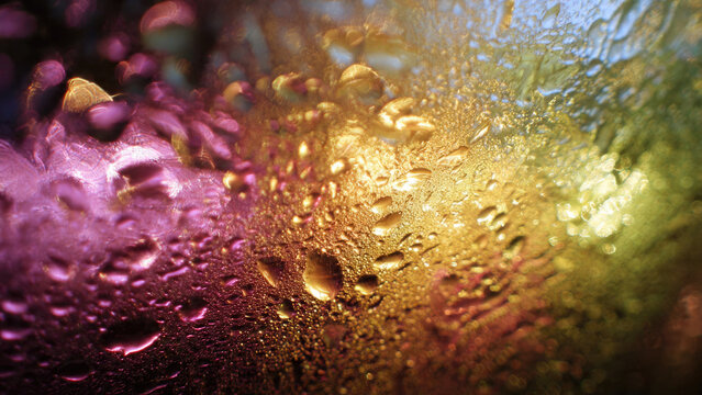 Mesmerizing water droplets cling to a surface, creating a vibrant abstract tapestry of blurred pink, gold, and green lights. Atmospheric and textural beauty.