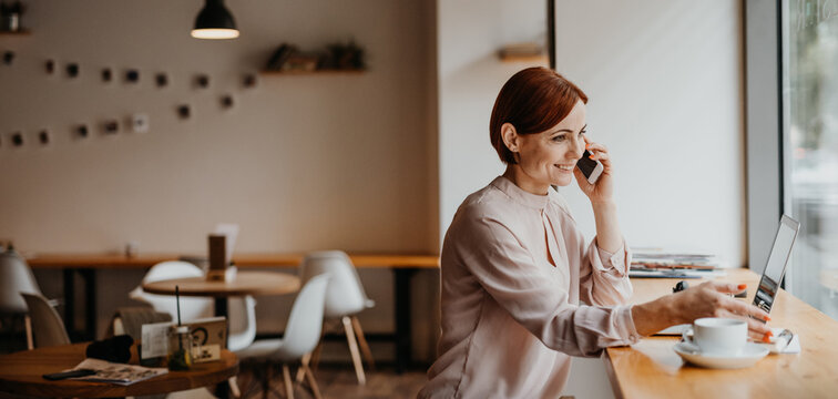 A portrait of woman working remotely from coffee shop, making phone call.