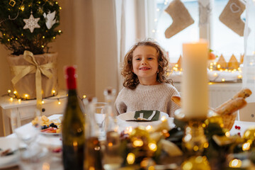 Cheerful small girl indoors at home at Christmas, looking at candle.