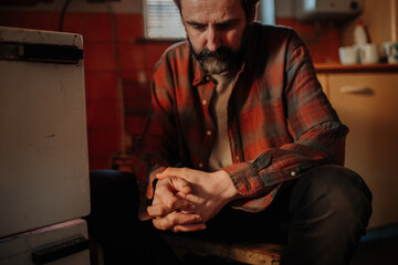 Despaired man sitting by wood stove in aged interior.