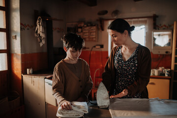 Mother ironing old clothes, daughter helping.