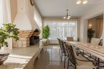 Bright and welcoming dining space featuring a large table, elegant chairs, and a fireplace. Sunlight streams in through large windows, creating a warm atmosphere