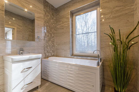A stylish bathroom showcases a bright and spacious design with a sleek bathtub, a contemporary sink, and a large window that allows natural light to enter, enhancing the tranquil atmosphere