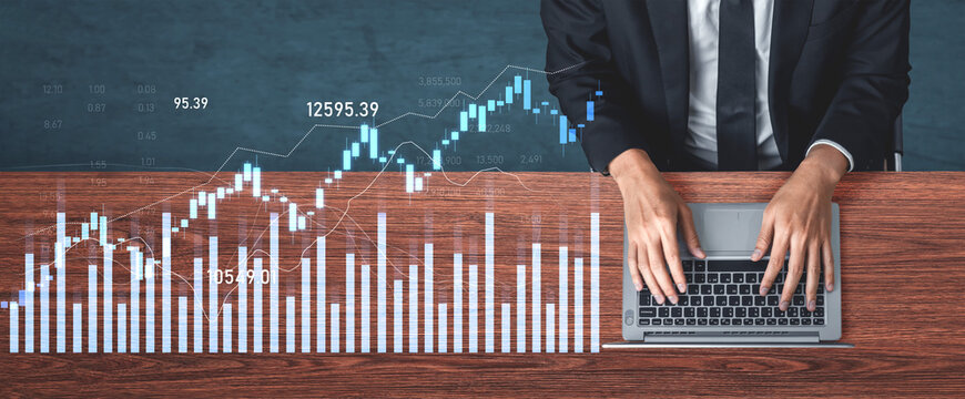 A business professional analyzes financial data on a laptop, with stock market graphs displayed on a wooden desk, illustrating modern workplace dynamics and investment strategies. Scalp