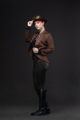 Stylish woman with short red hair in steampunk bowler hat with goggles on gray
