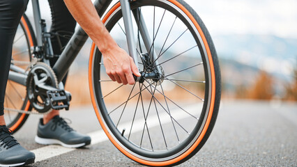 close up of a cyclist tightening the quick release on a road bike&rsquo;s front wheel while standing on an open road before riding