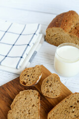 Rustic homemade bread sliced on a wooden board with a glass of milk on a bright white kitchen background. Fresh, cozy breakfast atmosphere with natural light and simple styling.