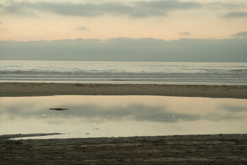 Large pool of reflective ocean water on empty beach in pacific beach
