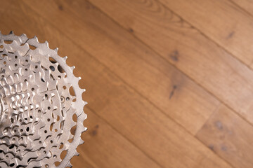 Close-up of a multi-sprocket bicycle cassette resting on wood flooring, showing gear progression and hub interface