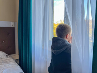 Boy looking out bedroom window feeling lonely and waiting