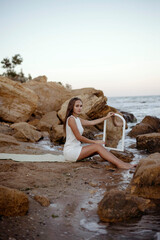 young, slender woman in a white dress walks barefoot on a sandy beach.