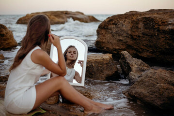 young, slender woman in a white dress walks barefoot on a sandy beach.