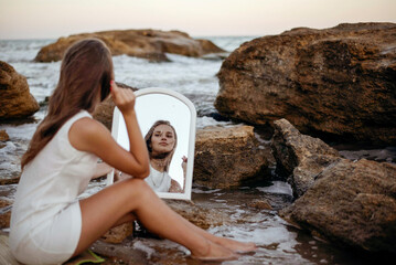 young, slender woman in a white dress walks barefoot on a sandy beach.