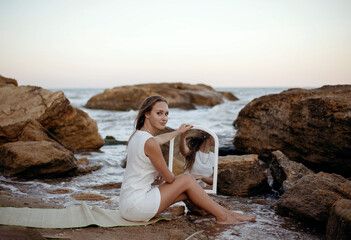 young, slender woman in a white dress walks barefoot on a sandy beach.
