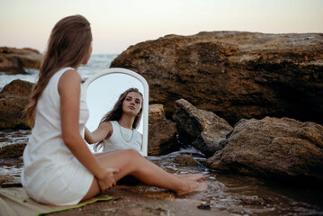 young, slender woman in a white dress walks barefoot on a sandy beach.