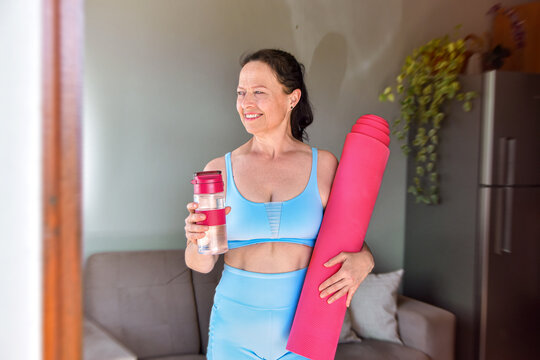 mulher madura com roupas fit segurando pr&eacute; treino garrafa de &aacute;gua e tapete de yoga, estilo de vida ativo e saud&aacute;vel