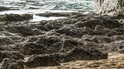 Jagged rocks along a coastal shoreline during rainfall. Ocean waves and stone wall add depth to this dramatic weather scene