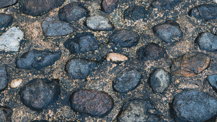 Irregular cobblestones in shades of gray and brown embedded in dark mortar. Textured paving ideal for historical or rustic design themes