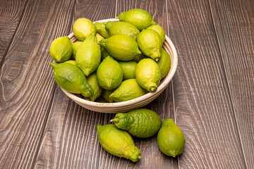 Fresh green lemons in a wicker bowl on wood