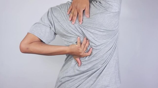 Back pain. A young man with back pain is touching and massaging his upper back. His shoulders are stiff and painful. Back injury, muscle pain, fatigue, health problems
