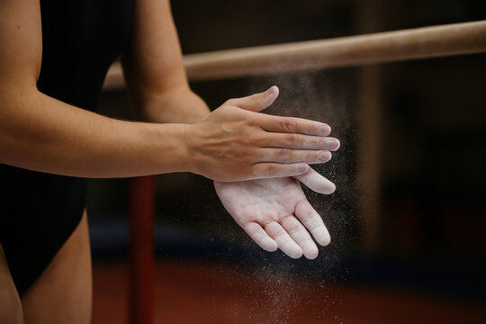 Preparing for the Next Performance: A gymnast's hands, coated in chalk, stand ready at the parallel bars, exuding focus and discipline before her routine.