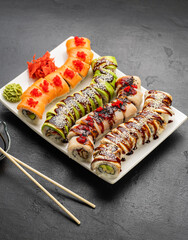 Assorted sushi rolls on platter with soy sauce, wasabi and ginger on black stone