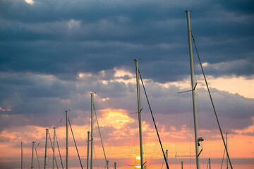 Sailboats masts reaching sunset sky with rigging