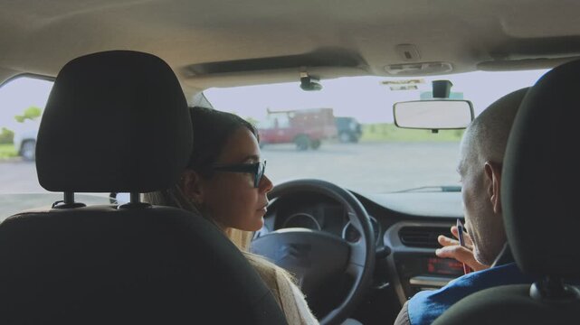Young woman practicing driving skills with an instructor taking notes during a driving lesson