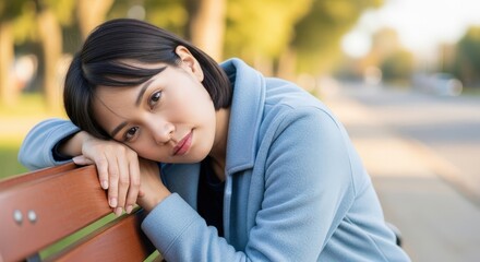 Fototapeta premium Young woman resting her head on a park bench and looking thoughtful 