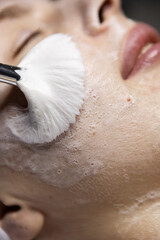 Fototapeta premium Close up of a facial cleansing procedure with a soft brush applying foaming cleanser to the woman skin during a professional skincare treatment.