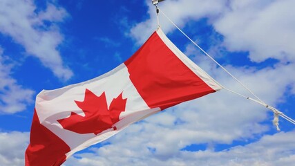 Slow motion footage of the Canadian flag blowing in the wind on a bright sunny day in Canada with a few clouds in the sky in the summer time